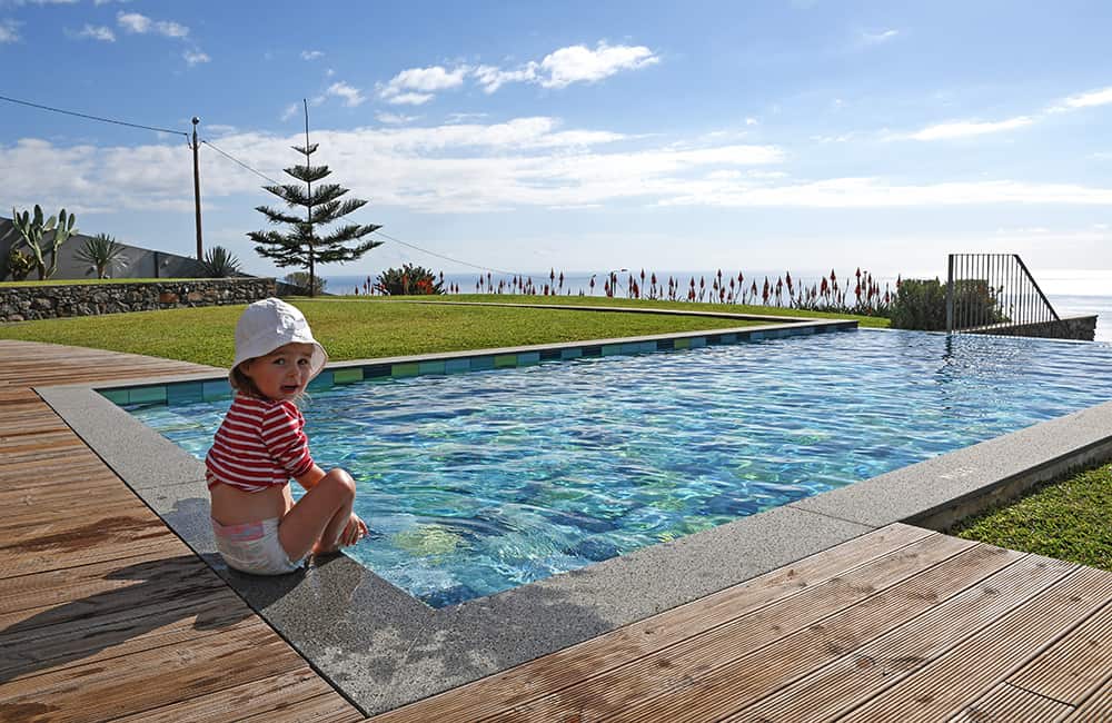 a little girl sitting at an infinity pool overlooking the ocean on the island Madeira