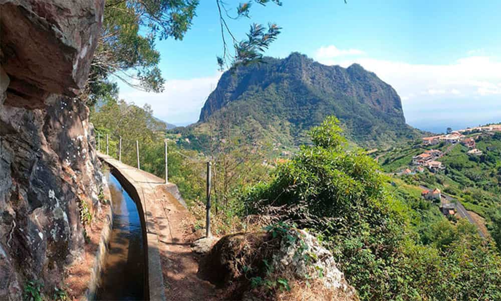 scene of an levada hiking trail on madeira with views down and over to the ocean on a sunny day
