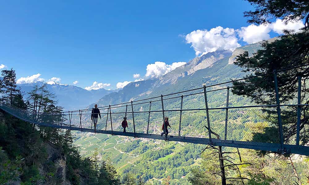 father with kids walking across the suspension bridge at torrent neuf a family friendly hike in Valais