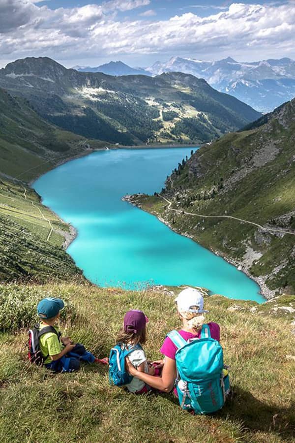 mother with 2 young kids sitting in a field overlooking cleuson dam in Valais on a family friendly hike