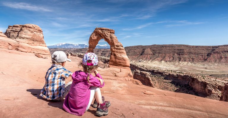 kids sitting in front of the delicate arch in arches national park