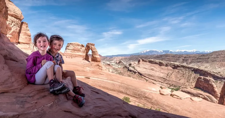children laughing and sitting on the secret window lookout overlooking the Delicate Arche in Moab