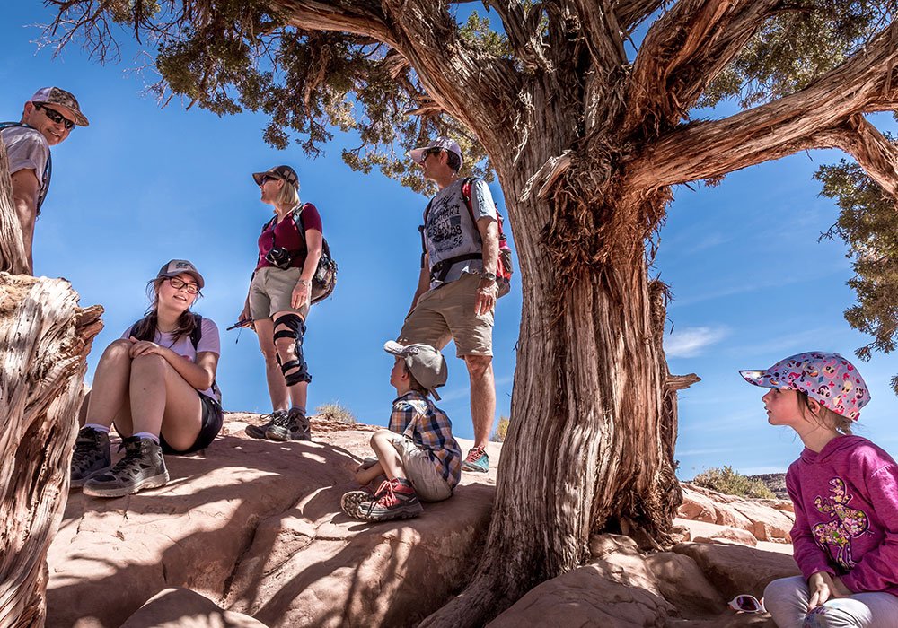 people standing under a shady tress whilst hiking delicate arch in Moab