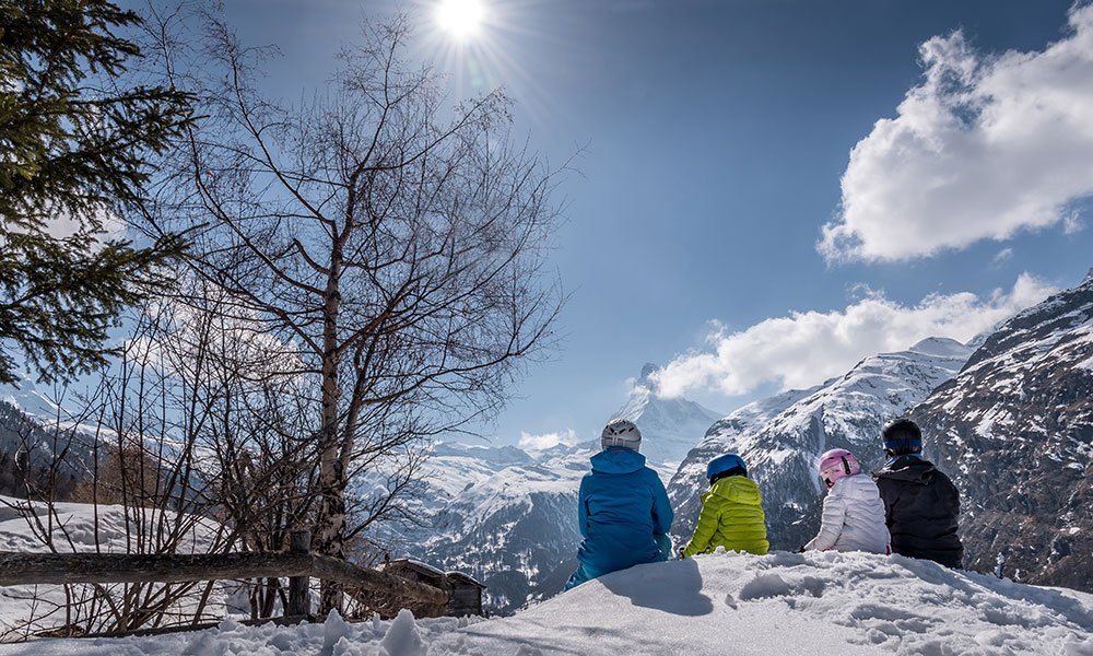Familie in Zermatt im Winter im Schnee sitzend mit Blick aufs Matterhorn