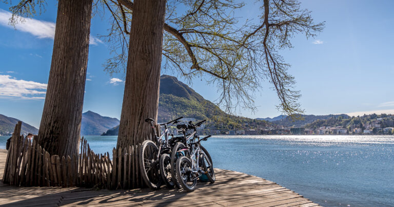 Family biking along Lake Lugano with view of Monte San Salvatore and Lugano Bay in Ticino Switzerland