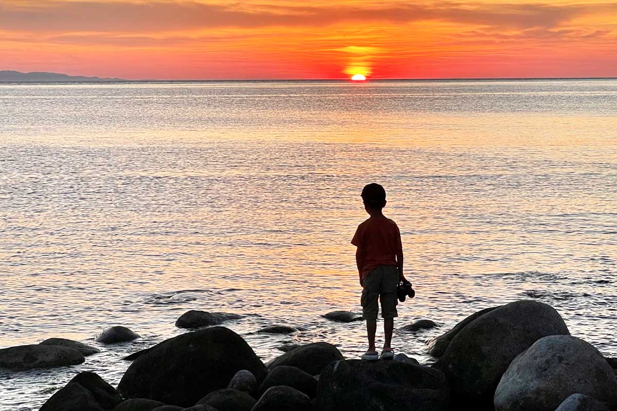 a little boy stands at the beach in Elba looking at the sunset