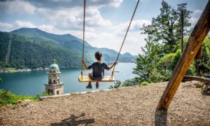 Boy sitting on the swing overlooking Morcote and Lake Lugano in Ticino Switzerland