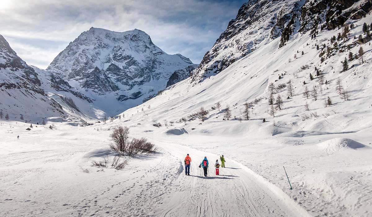 a family in winter hiking towards a snowy mountain and the Glacier cave in Arolla Switzerland