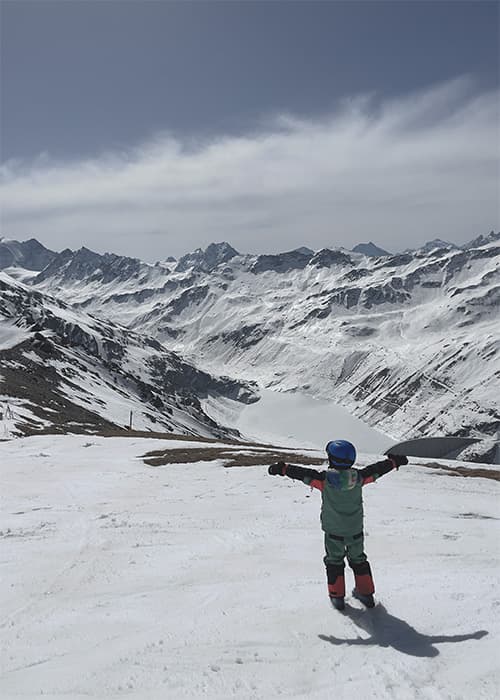 a little boy standing on top of a swiss mountain in val d'Anniviers looking at lac de Moiry
