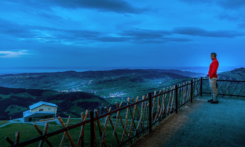 a man standing at the Ebenalp in the night looking down over Appenzell
