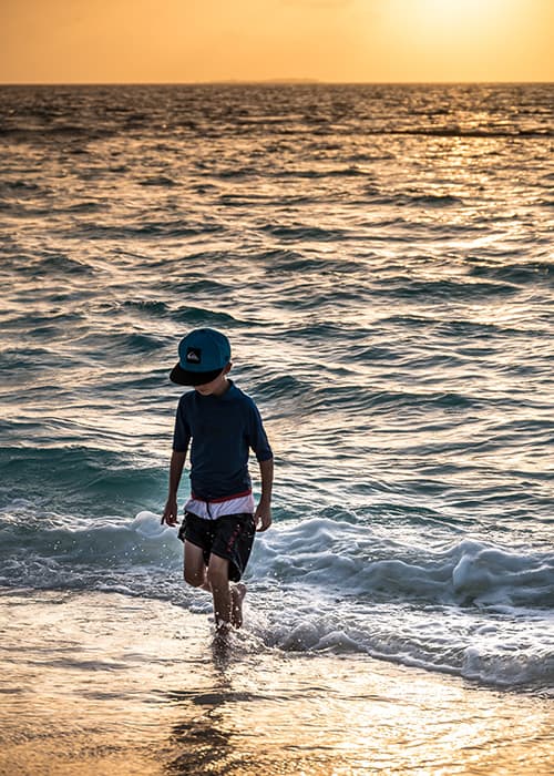 a boy walking at sunset out of the waters in the maldives