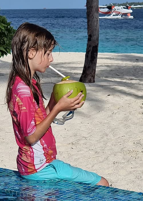 a girl driking a coconut at the pool at Reethi Faru resort maldives