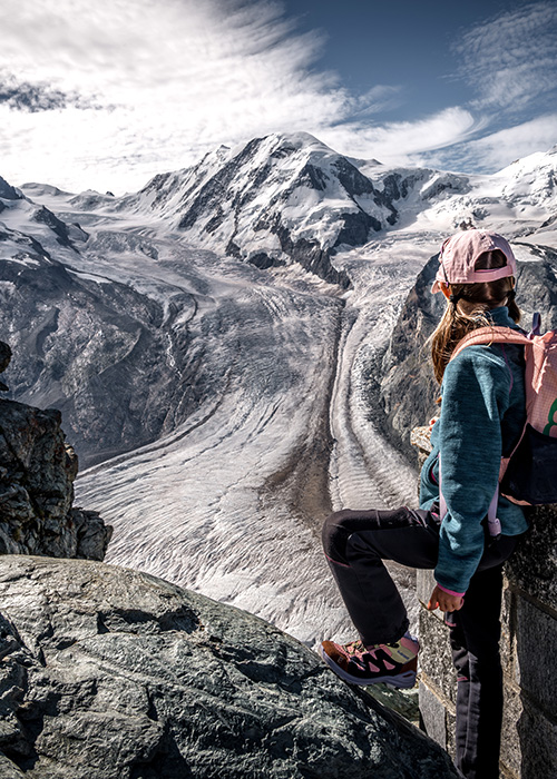 a girl standing at a viewpoint overlooking a glacier in zermatt