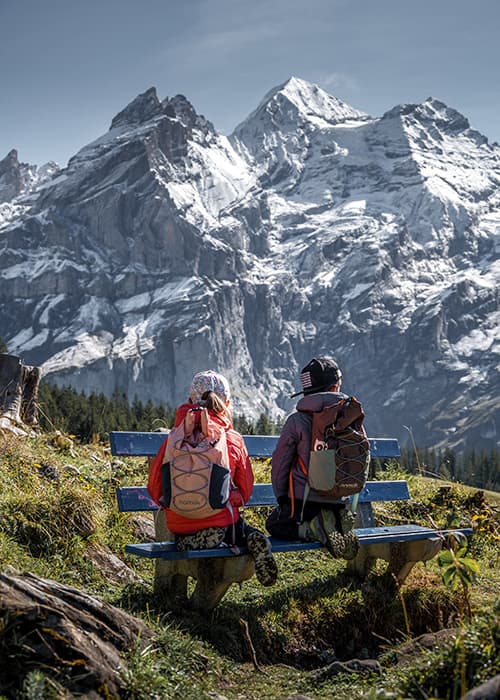 children sitting on a bench with Namuk bags and watching the mountains at oeschinensee