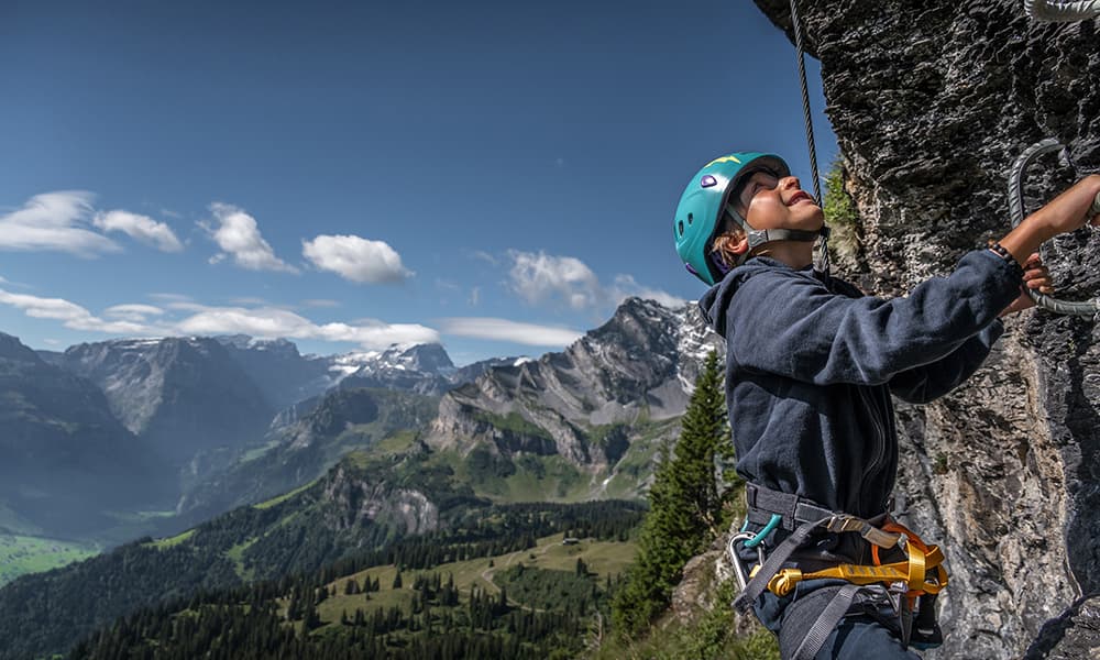 a boy on a climbing wall with mountains in the back in Braunwald