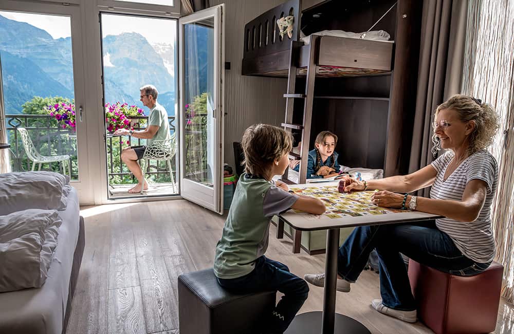 a family playing a board game, reading and sitting on a balcony in a hotel room of the Märchenhotel in Braunwald