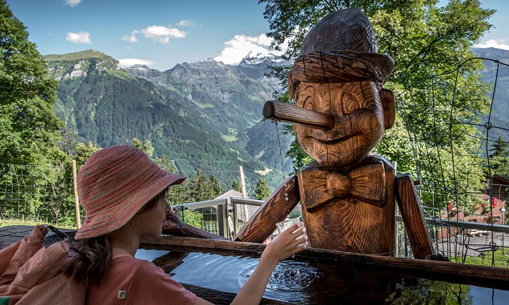 a wooden Pinocchio fountain with a girl standing in front