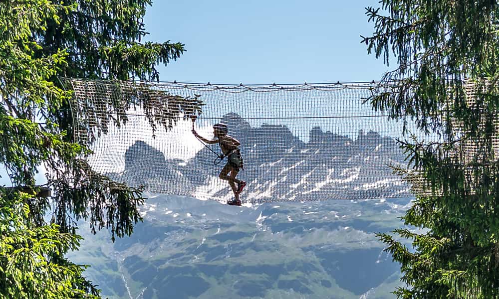 a girl in Braunwald at the Seilpark crossing a net with stunning mountains in the background