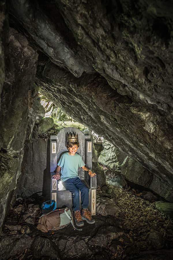 a boy sitting on a brown found in a cave whilst hiking in Braunwald