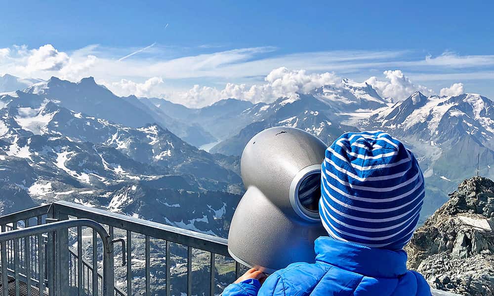 a small boy in a blue jacket looking through a mountain finder glass at 3300m on the Mont Fort in Switzerland
