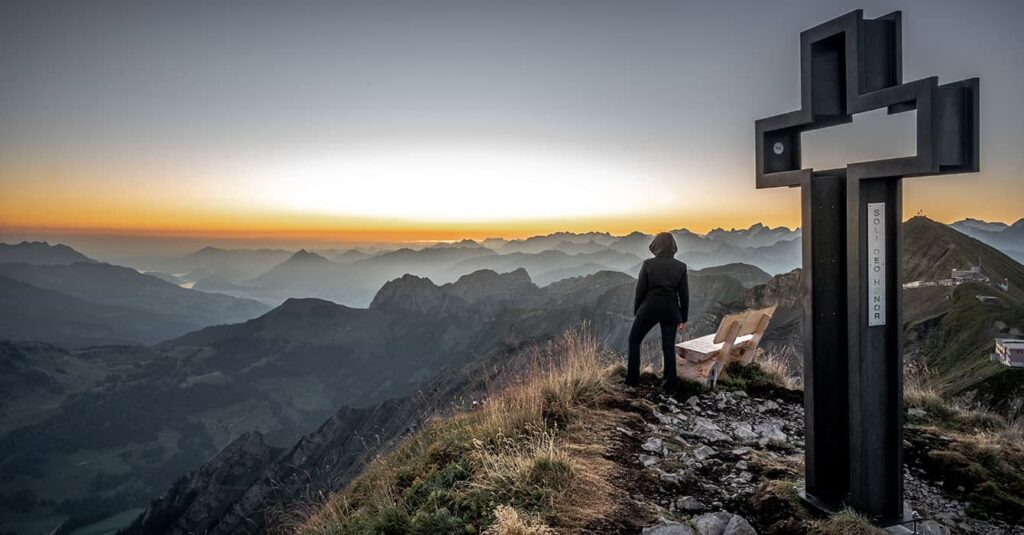 a woman standing by a cross in Switzerland at sunrise