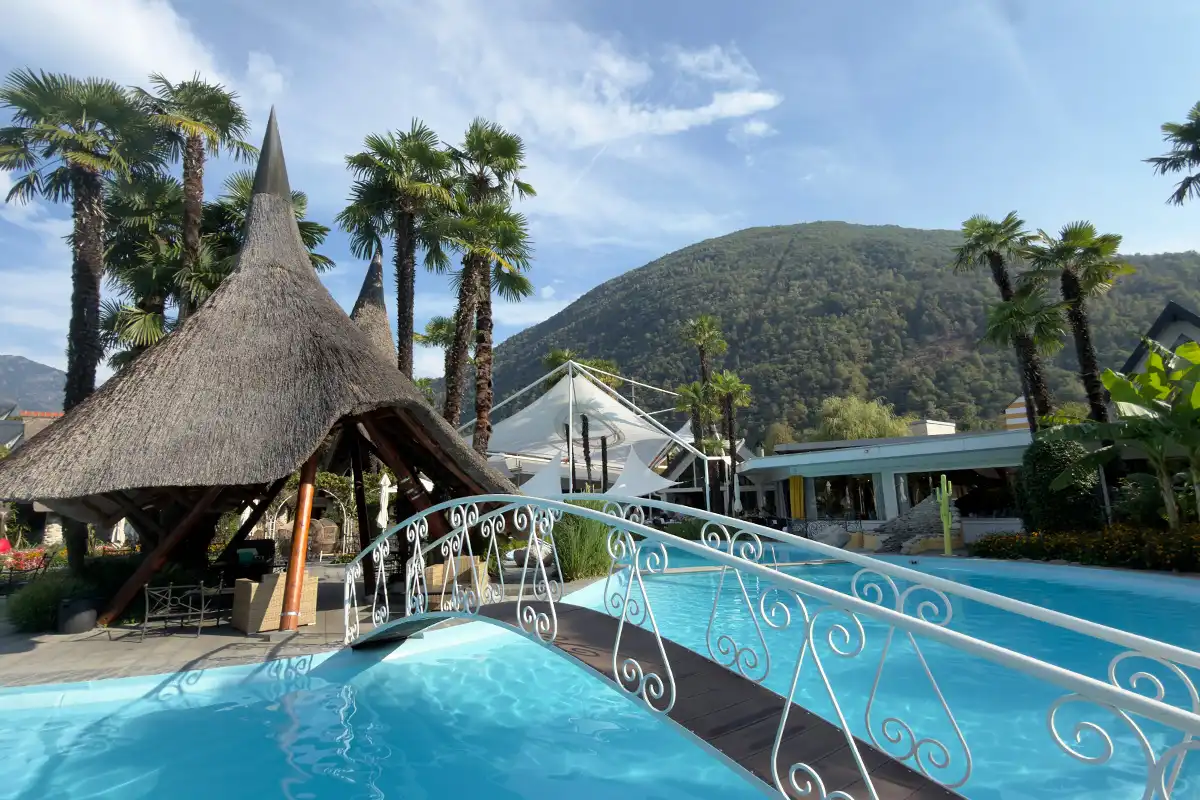 Pool area at Albergo Losone with plam tress , blue water and a bridge crossing the pool