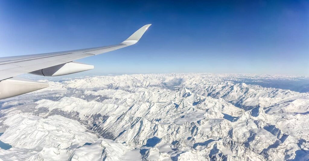 Airplane wing flying over snow-capped Alps between the UK and Switzerland