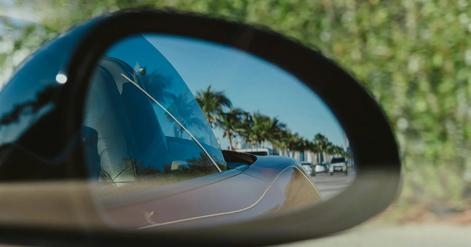 luxury car side mirror reflection palm trees and road in Dubai