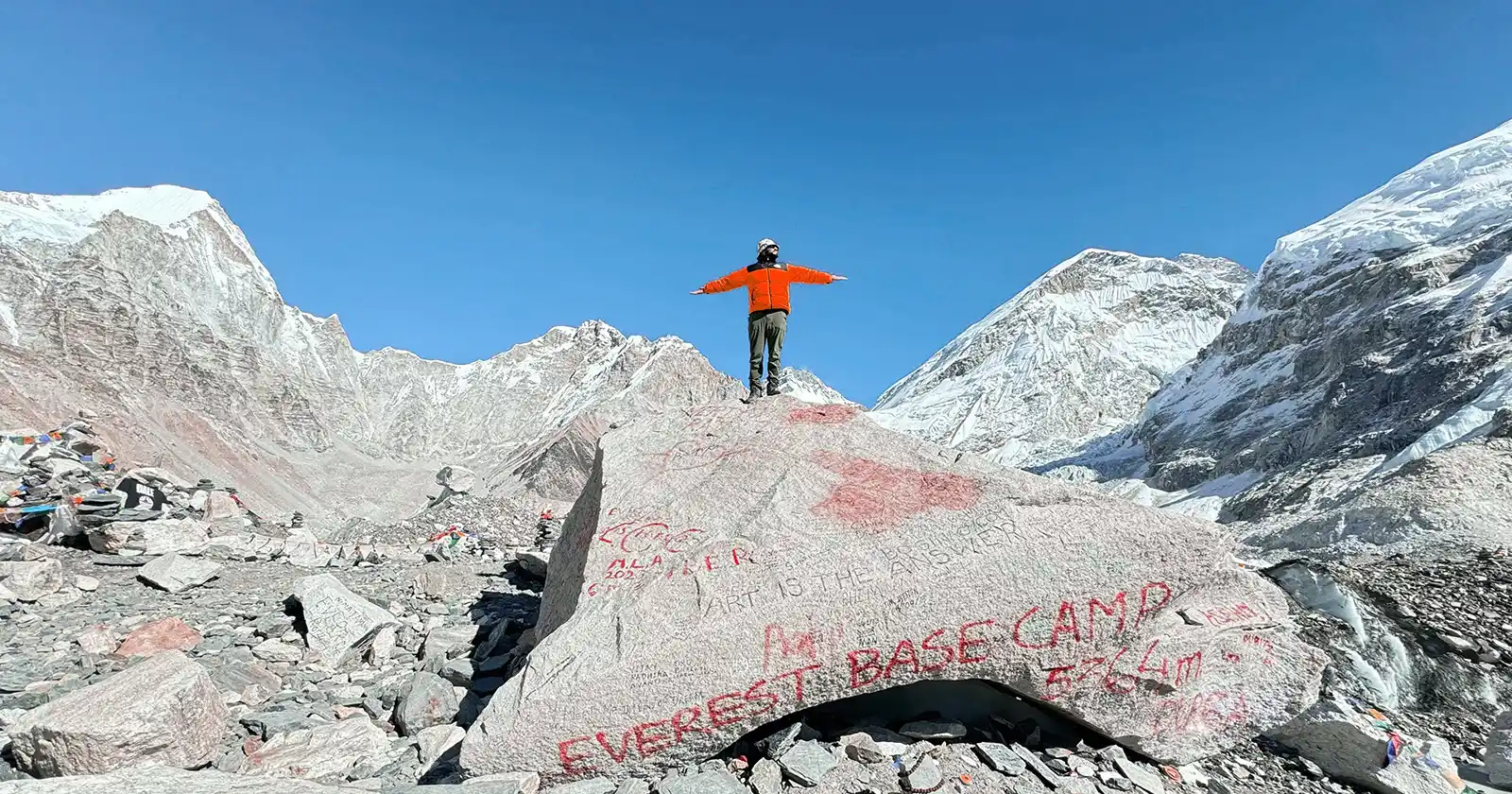 A man in a red jacket standing at Everest base Camp after the long trek in Nepal.